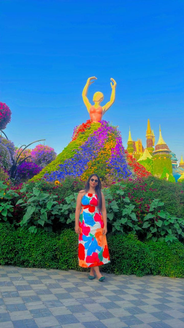 Woman in a colorful dress standing in front of a floral sculpture with a castle-like structure in the background.
