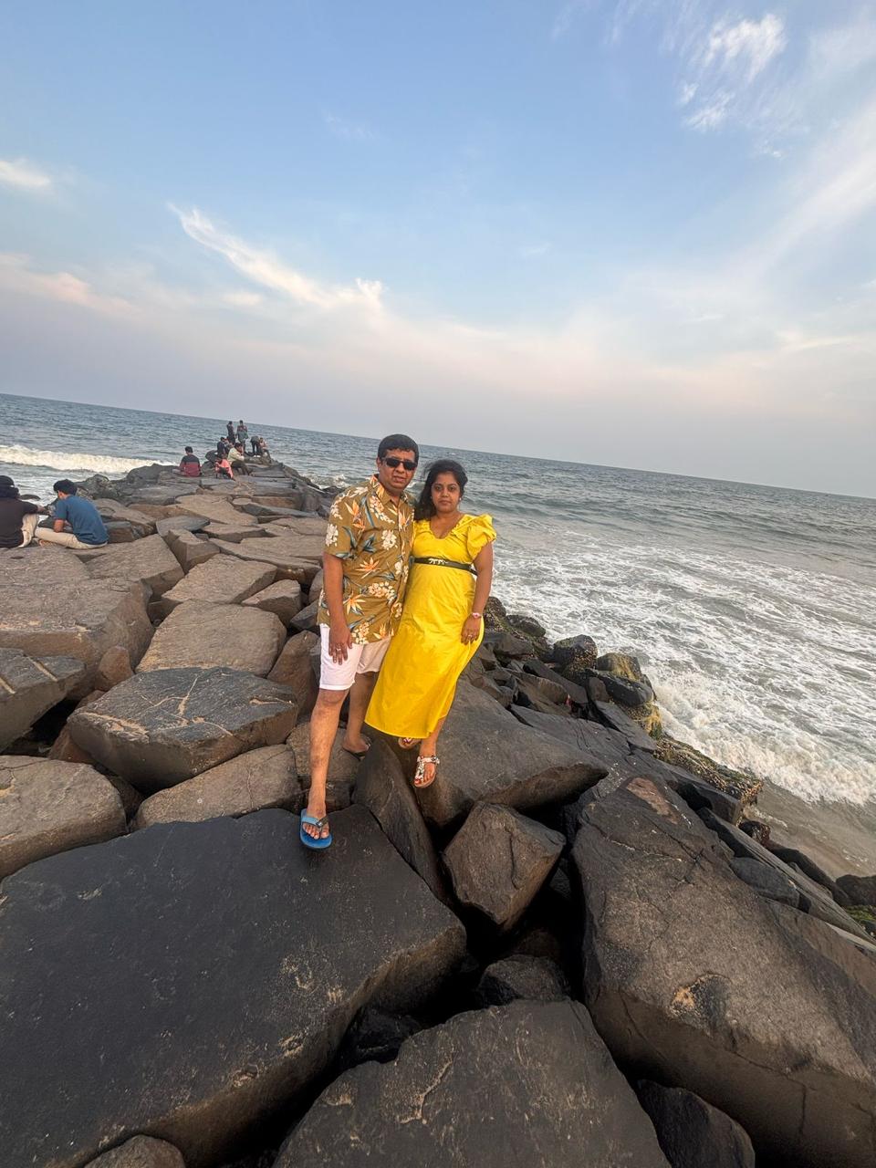 Two people standing on a rocky jetty by the ocean with a clear sky.