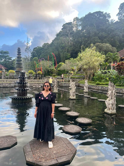 Woman in a black dress standing in front of a temple complex with water features and statues.