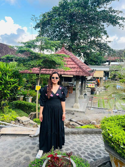Woman in a black dress standing in a garden with traditional architecture in the background