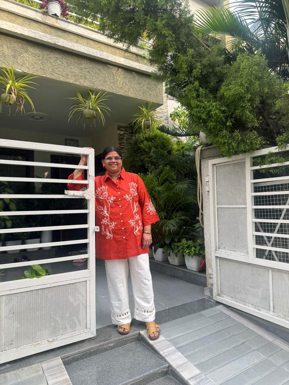 Person in a red shirt standing in front of a modern house entrance with plants.