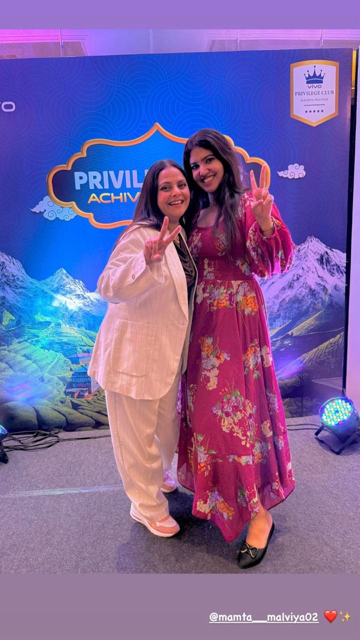 Two women posing in front of a Privil Achieve backdrop with scenic mountains.