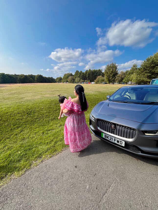 Woman in a pink dress holding a child next to a blue car on a sunny day.