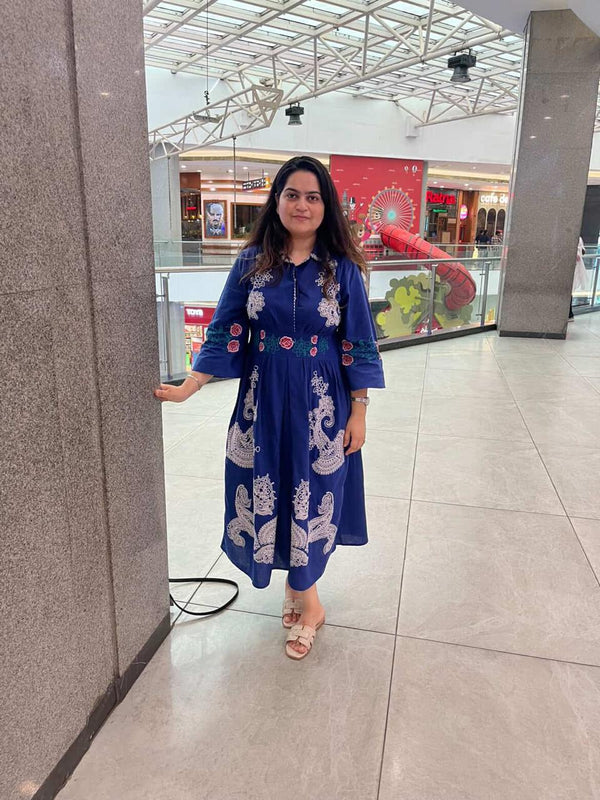 Woman in a blue dress with white patterns standing in a mall.