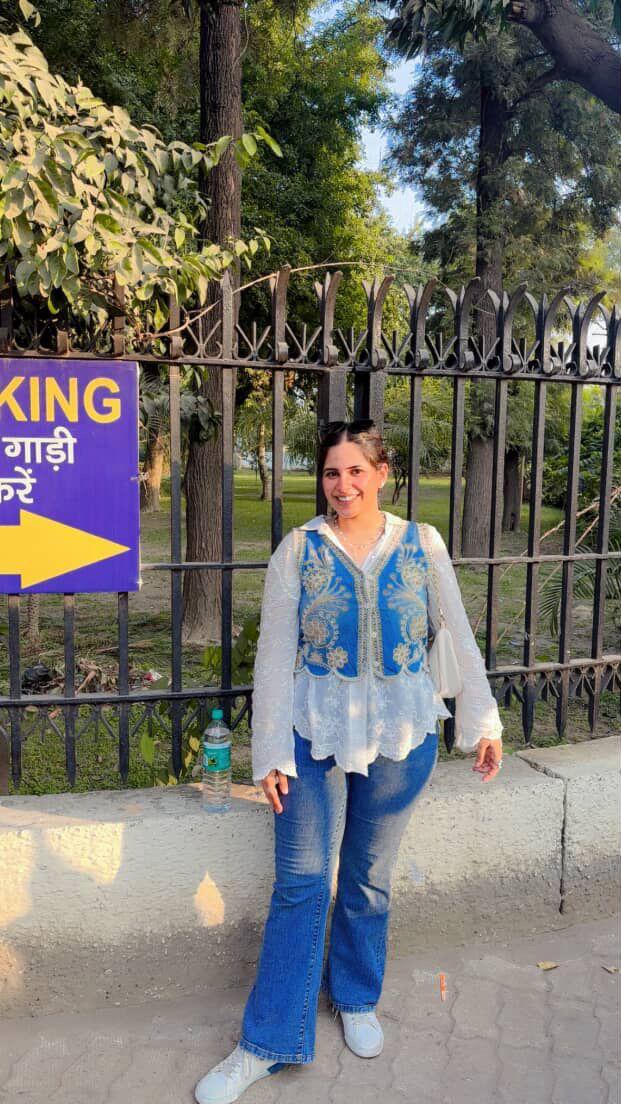 Woman standing in front of a gate with trees and a signboard in the background