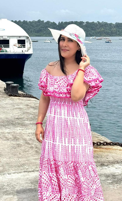 Woman in a pink dress and white hat by a waterfront with boats in the background