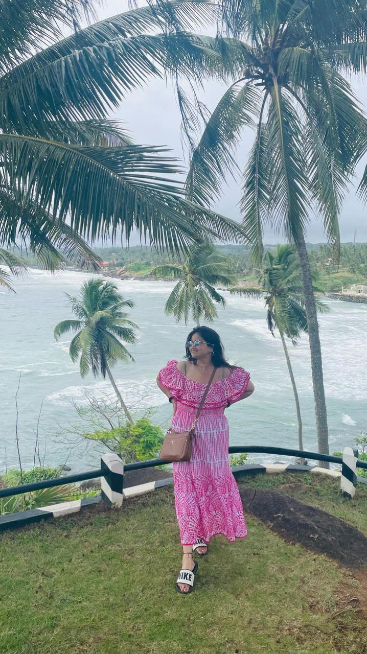 Woman in a pink dress standing by a body of water with palm trees in the background