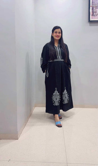 Woman wearing a black outfit with white embroidery in an indoor setting