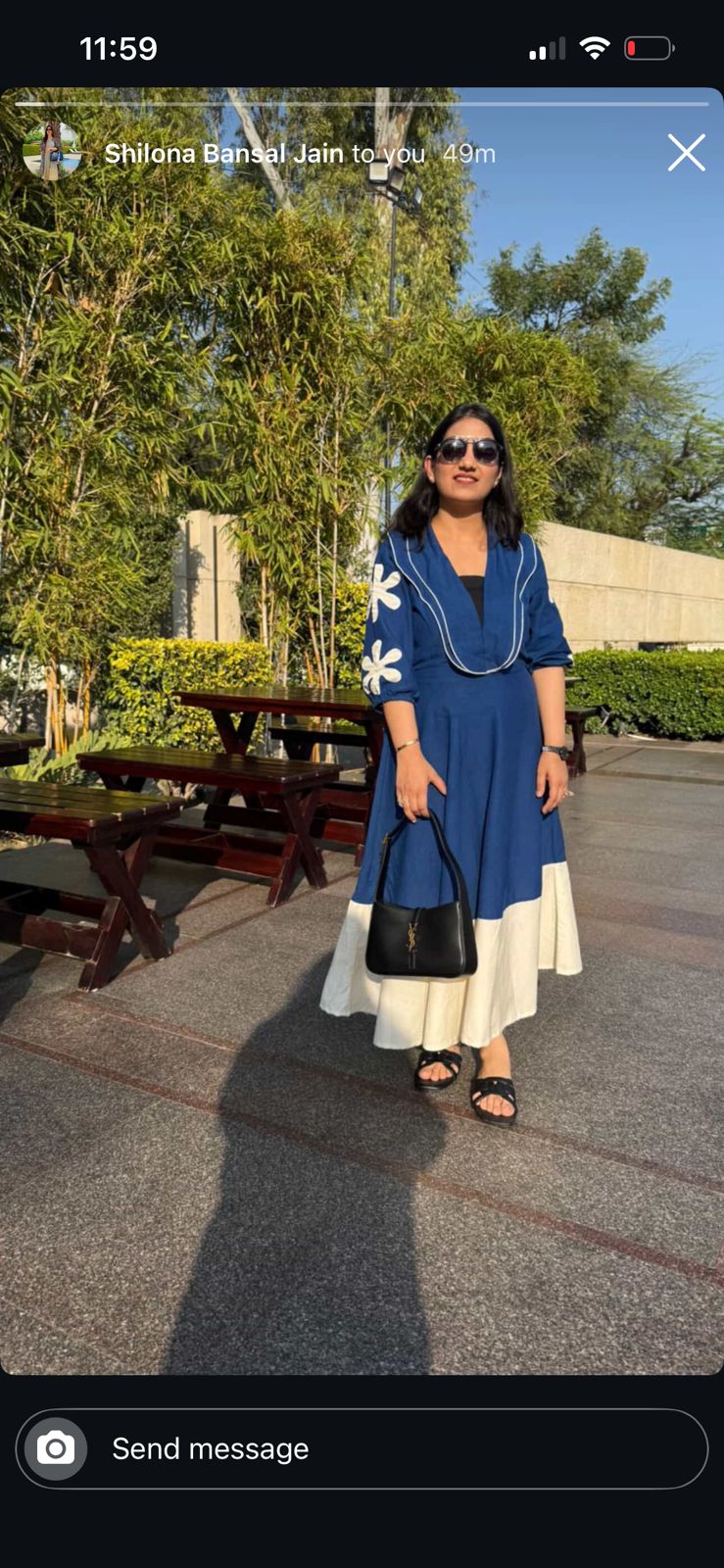 Woman in a blue dress standing outdoors with trees and a building in the background