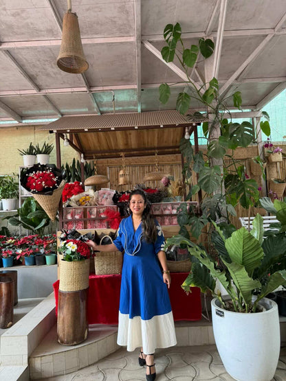 Woman in a blue dress standing in a floral shop with plants and flowers around.