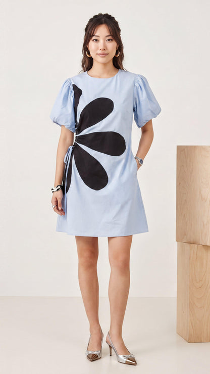 Woman wearing a light blue dress with a black flower design on a white background