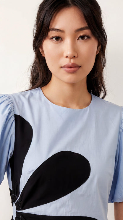 Woman wearing a light blue top with black abstract design against a white background