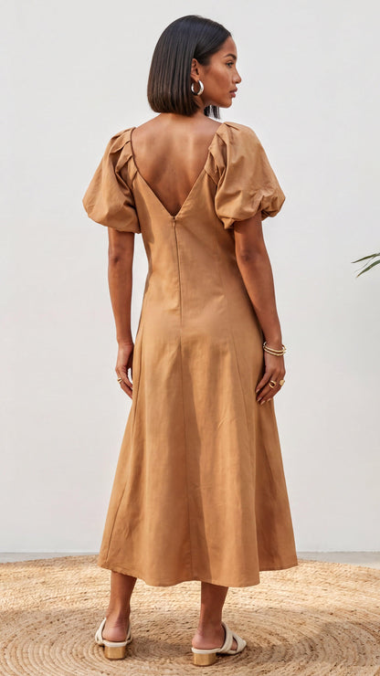 Woman wearing a tan dress with puff sleeves against a neutral background