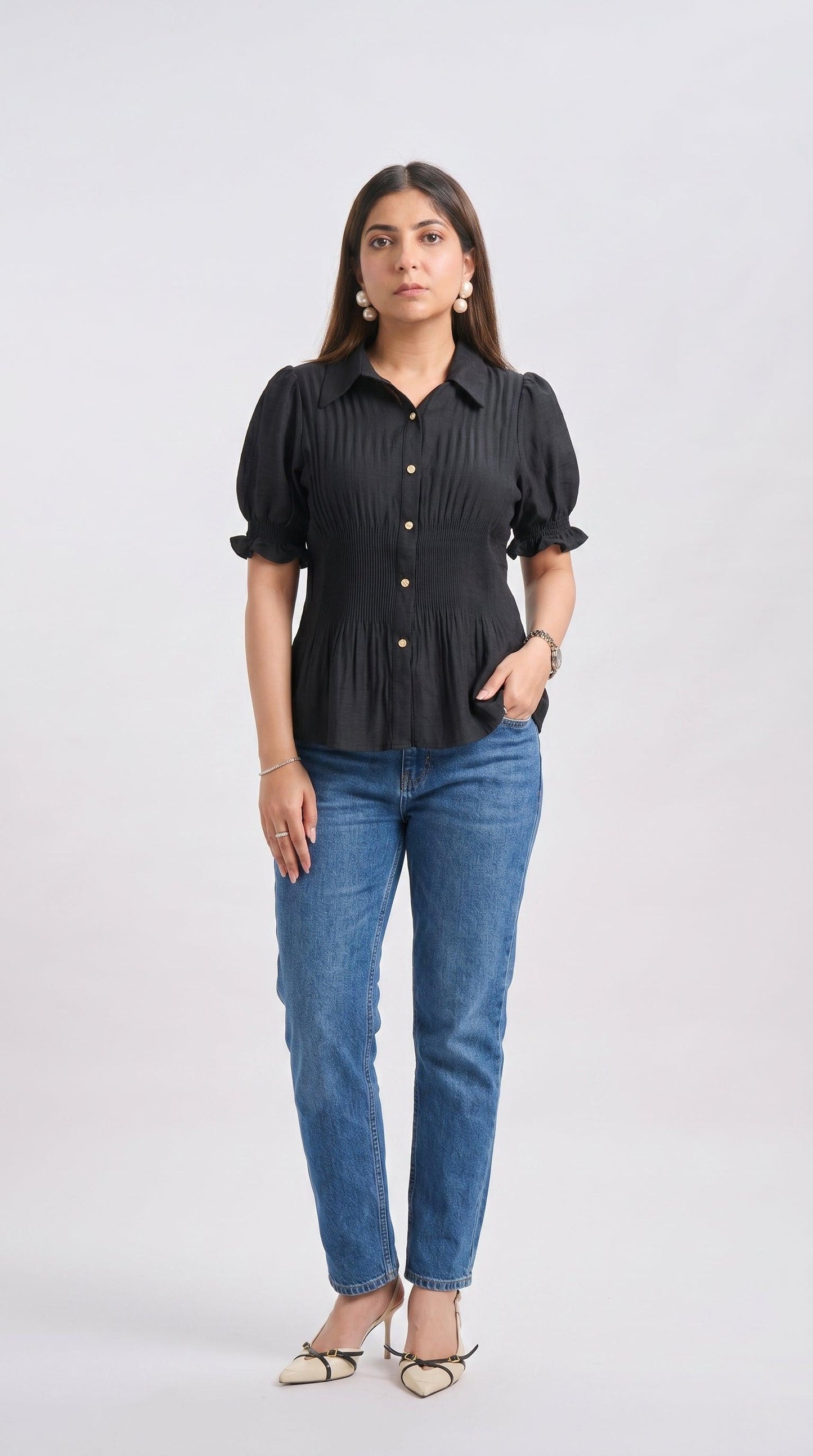 Woman wearing a black ruffled blouse and blue jeans on a white background
