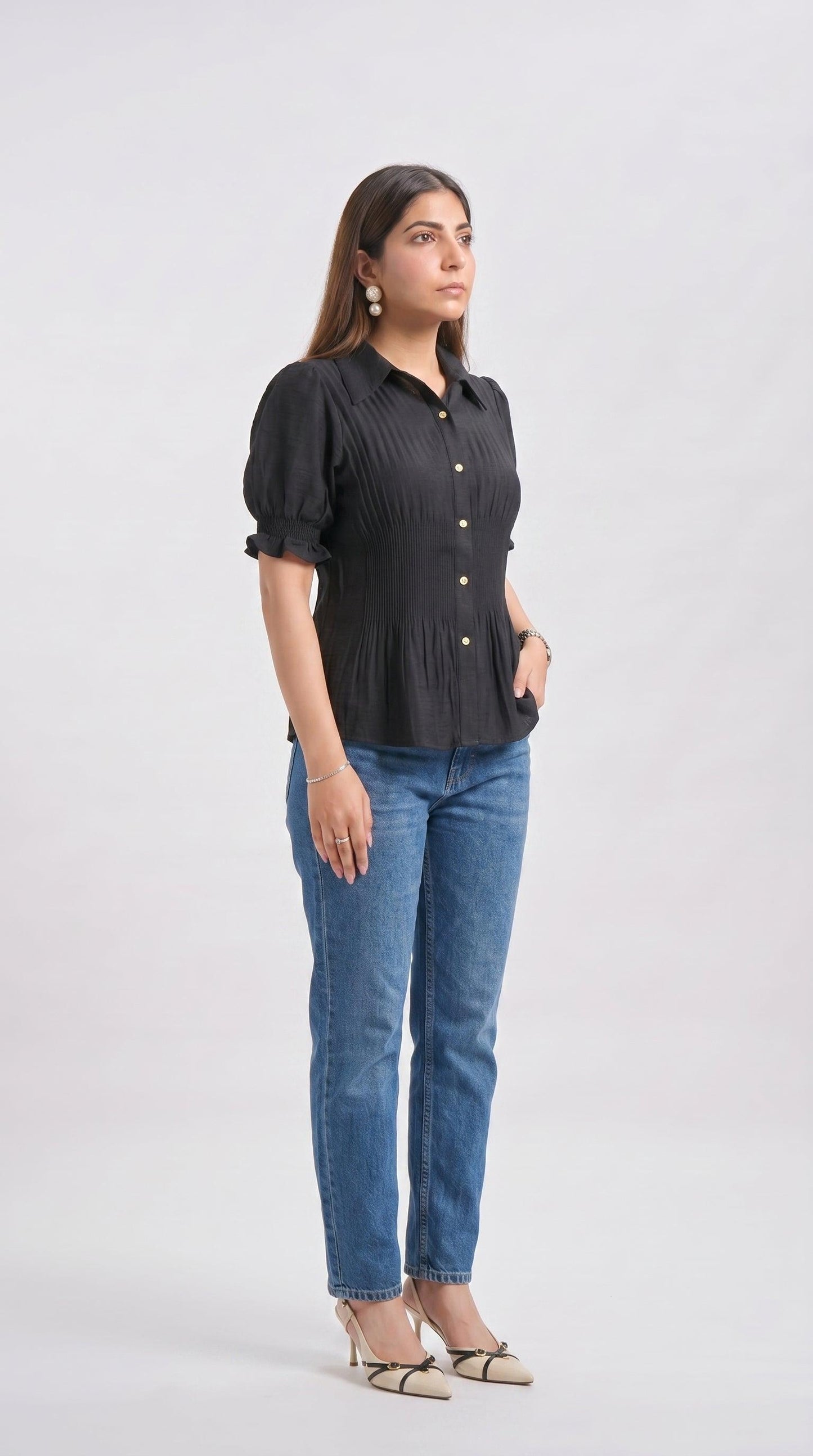Woman wearing a black blouse with puff sleeves and blue jeans on a white background