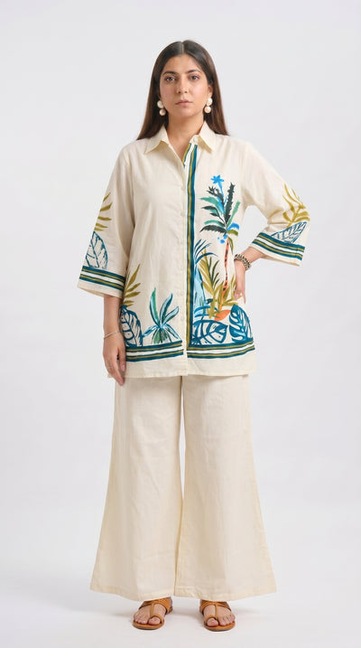 Woman wearing a cream outfit with floral embroidery on a white background