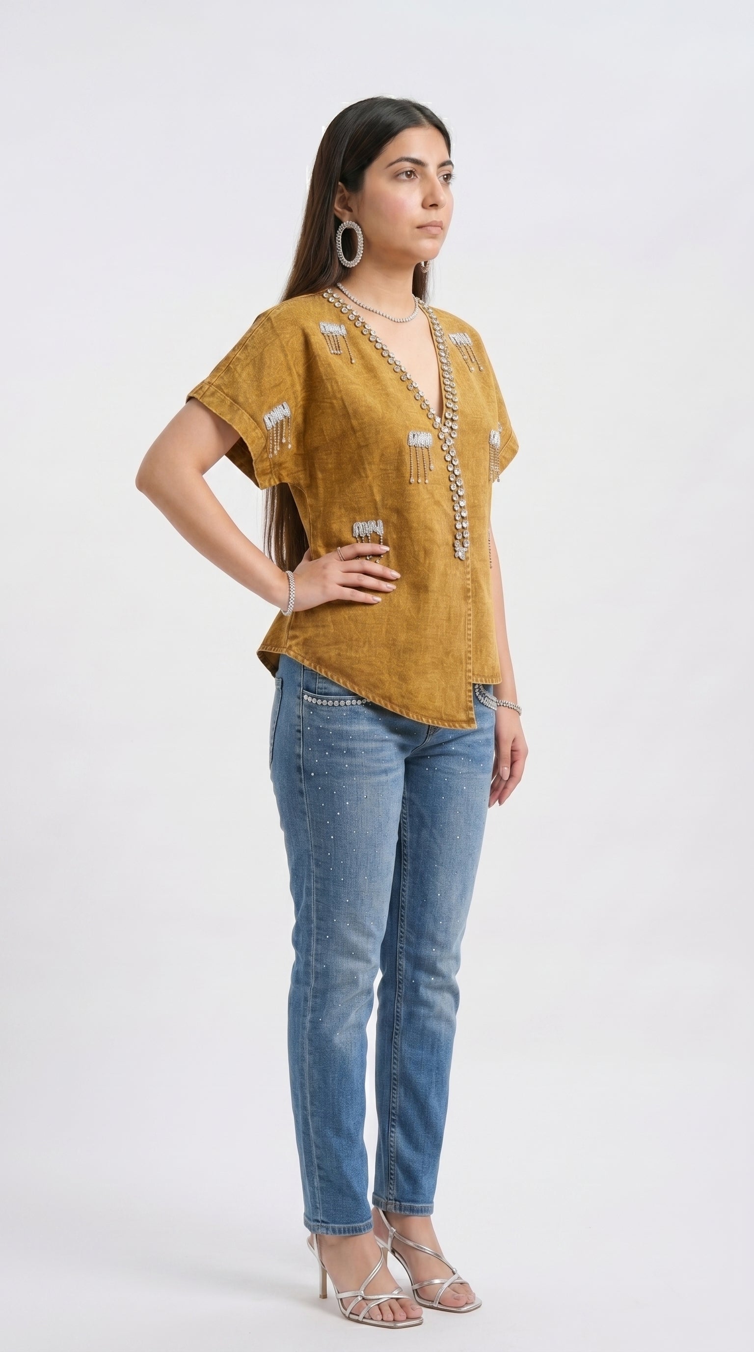 Woman wearing a mustard yellow top and blue jeans on a white background