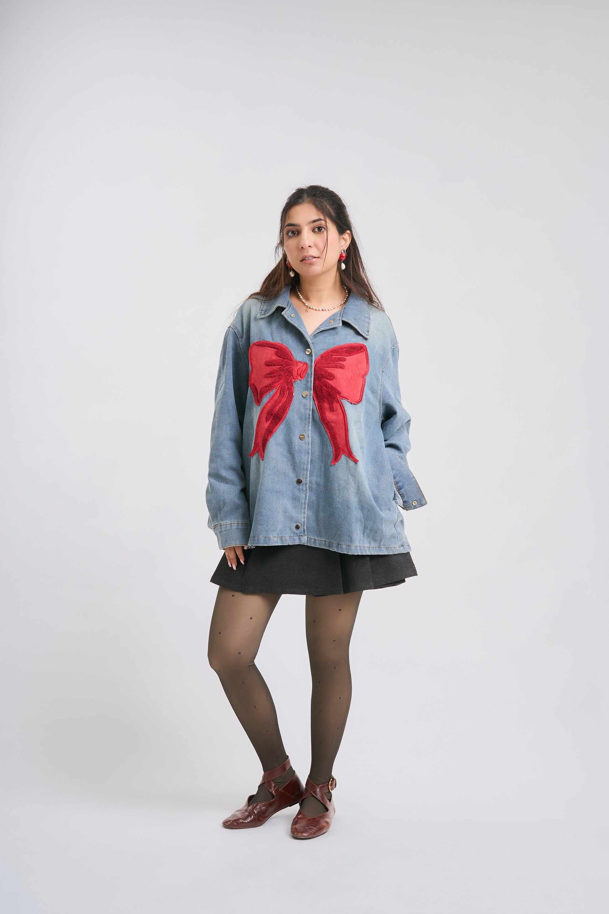 Woman wearing a denim jacket with a large red bow on a white background