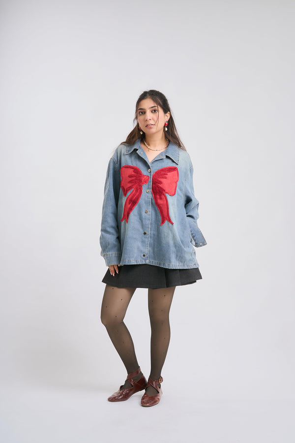 Woman wearing a denim jacket with a large red bow on a white background