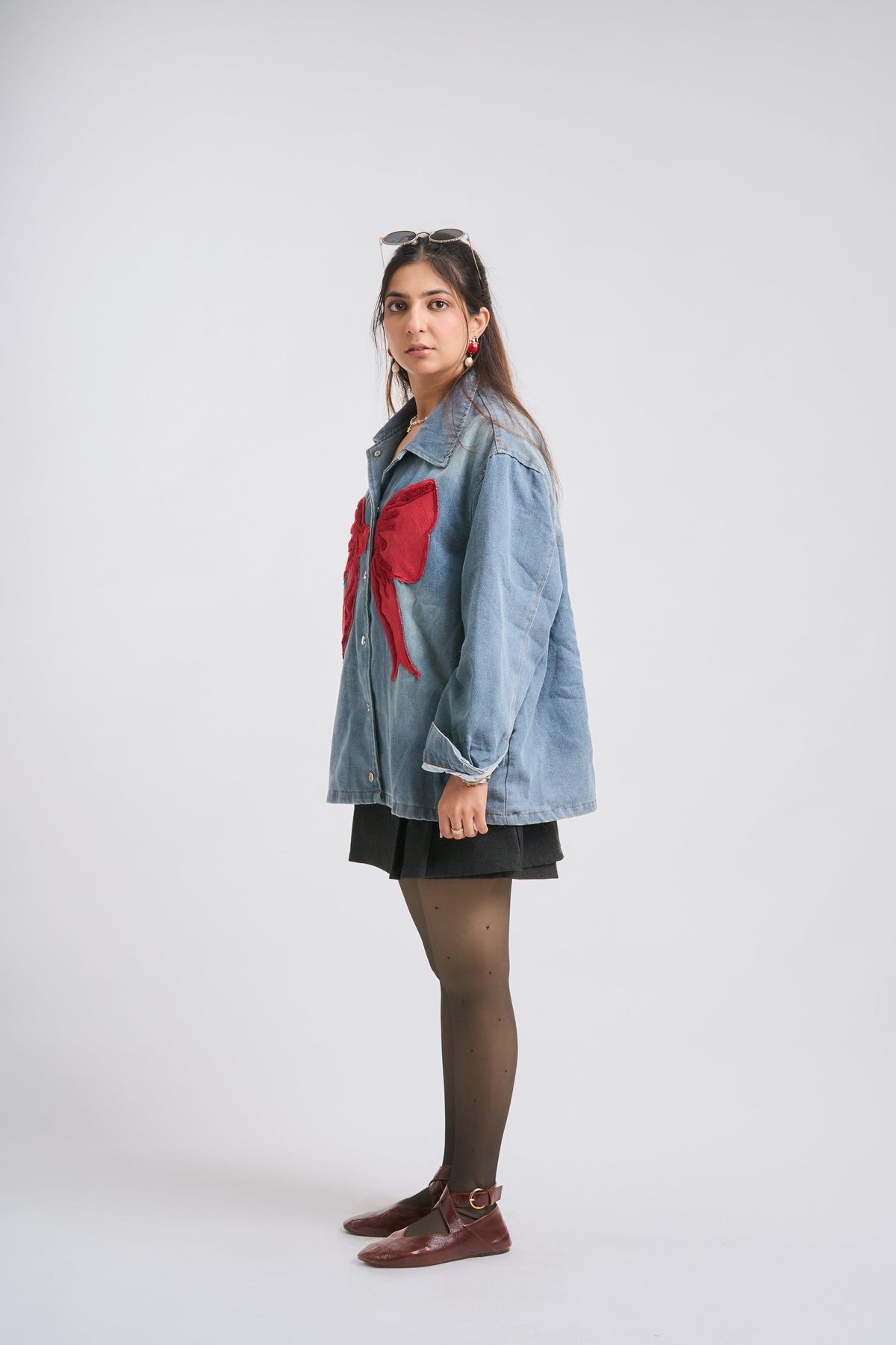 Woman wearing a denim jacket with a red bow, standing against a white background