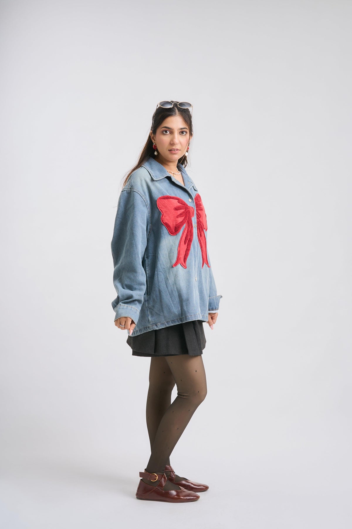 Woman wearing a denim shirt with a red bow and black skirt on a white background