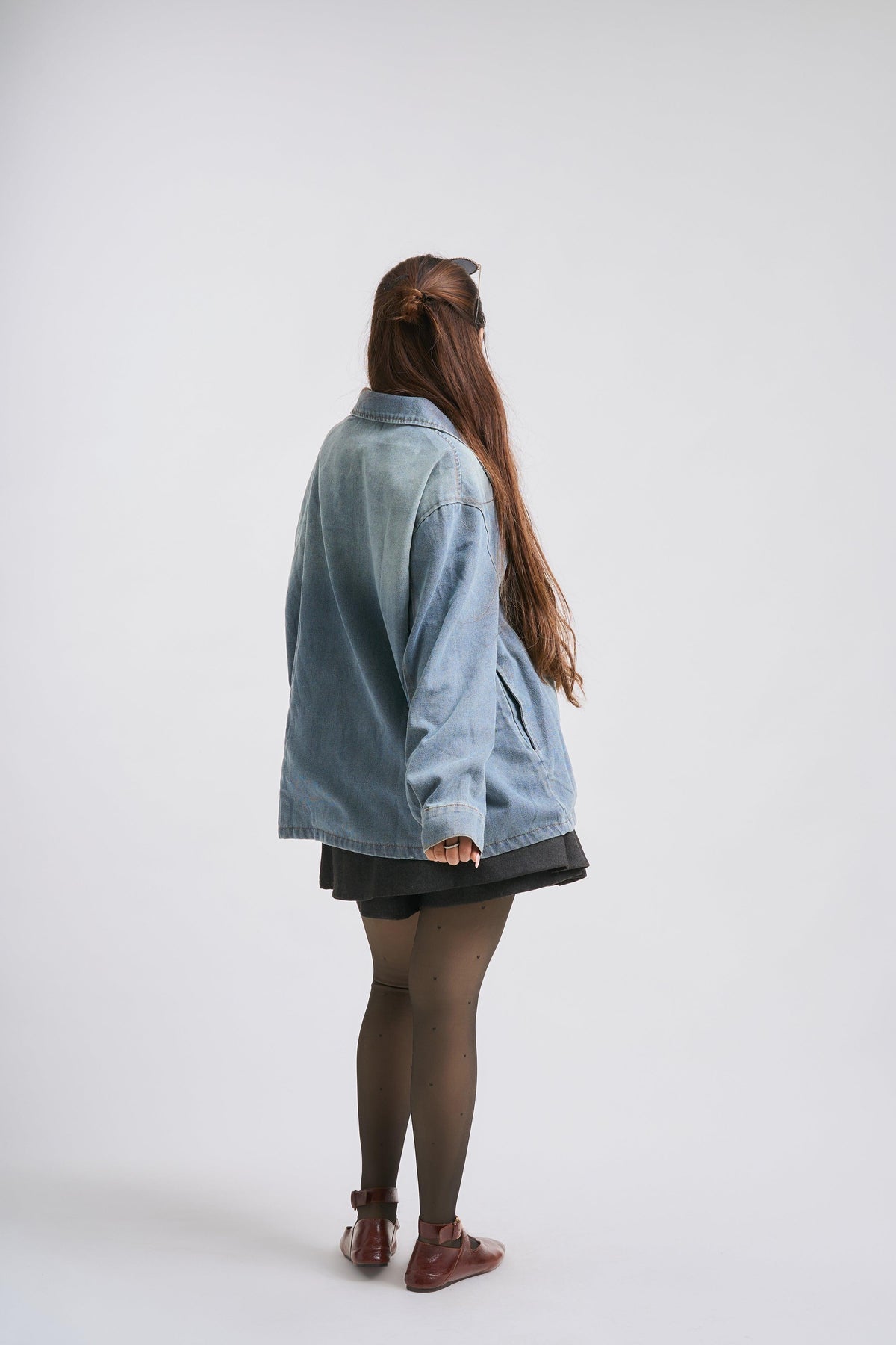 Person wearing a light blue denim jacket on a white background