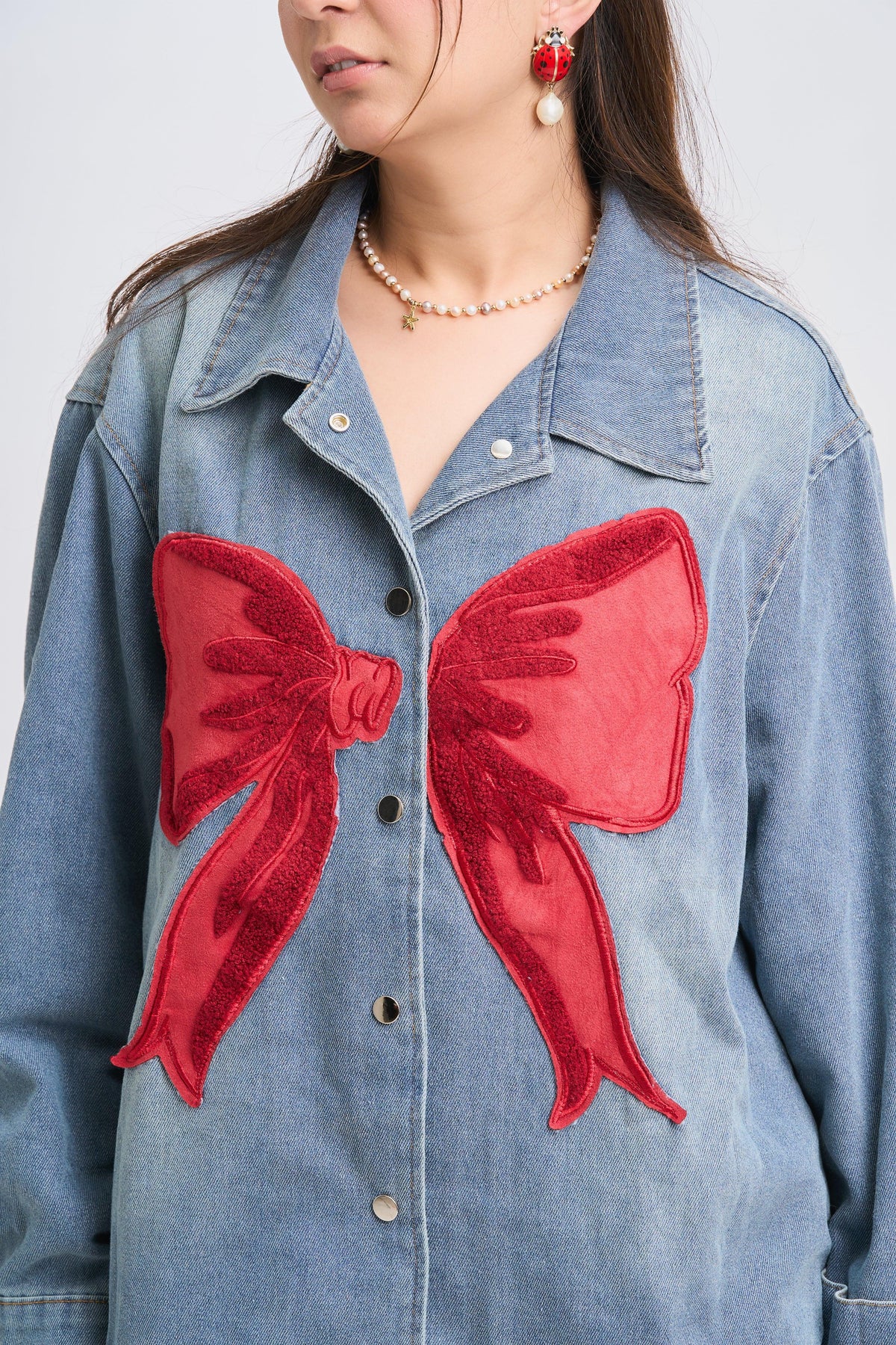 Denim jacket with red bow patches worn by a person against a plain background