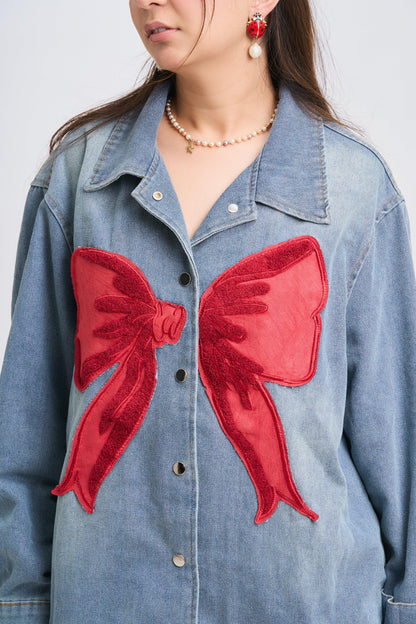 Denim jacket with red bow patches worn by a person against a plain background
