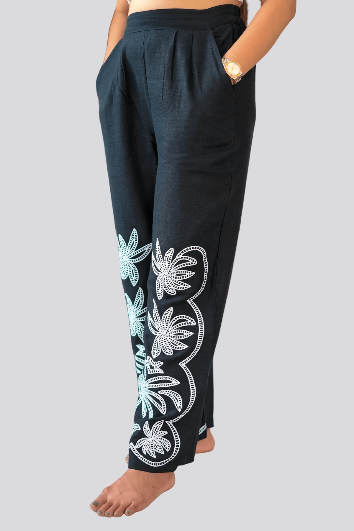 Black pants with white floral embroidery worn by a person, with a plant in the background.