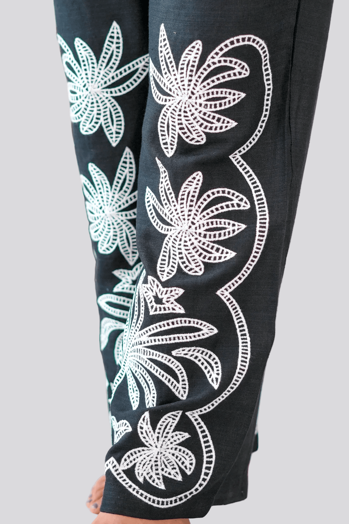 Black pants with white floral patterns worn by a person indoors.