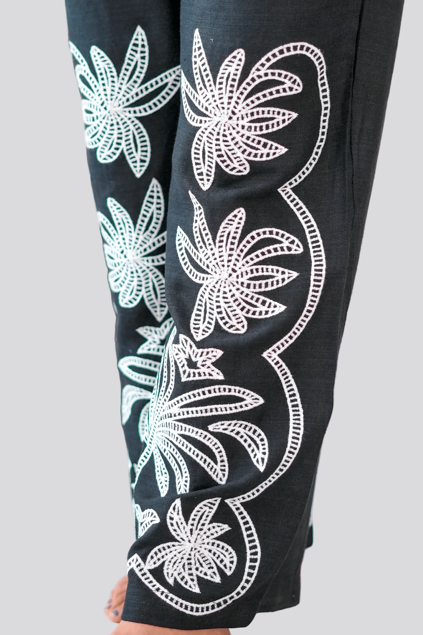 Black pants with white floral patterns worn by a person indoors.