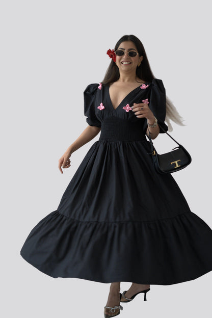 Woman wearing a black dress with pink floral accents against a white background