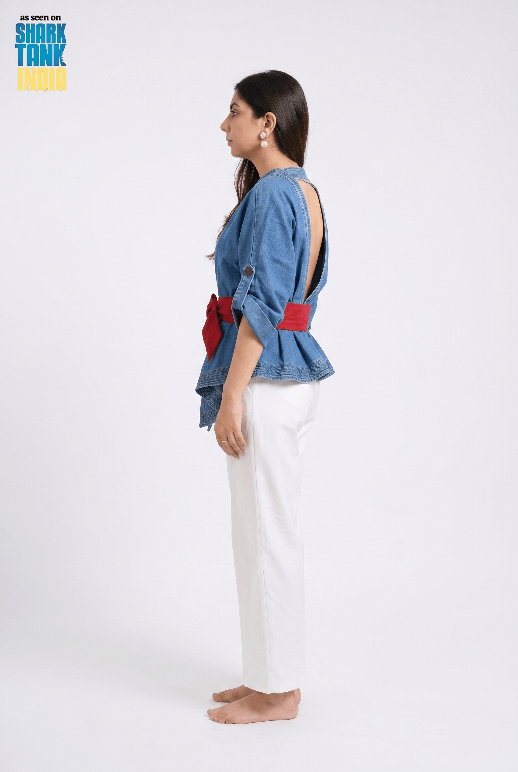 Woman wearing a denim top with red accents and white pants on a white background