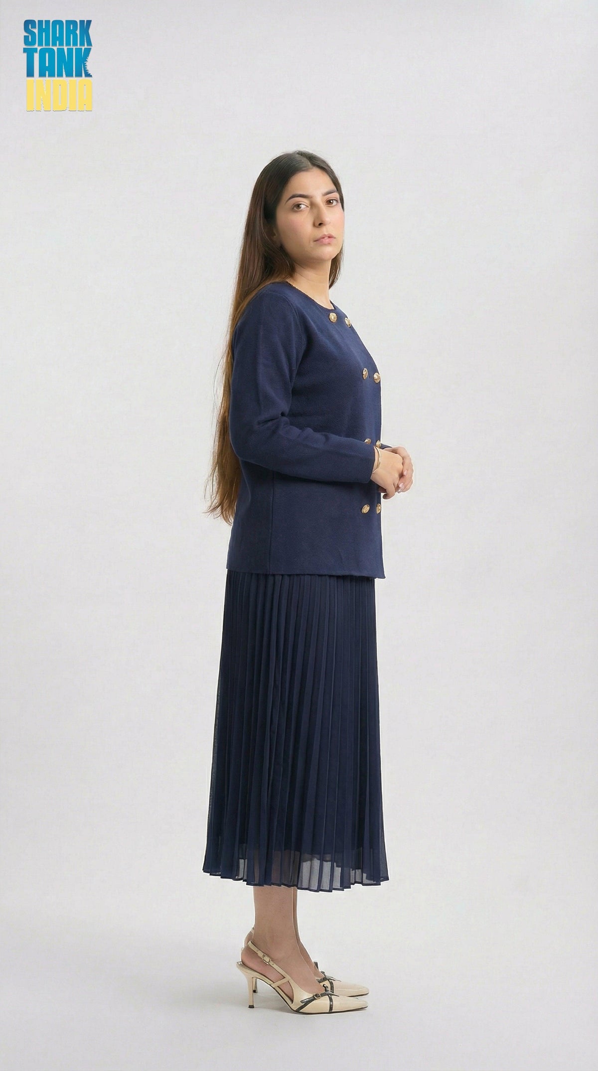 Woman wearing a navy blue outfit with a jacket and pleated skirt on a white background