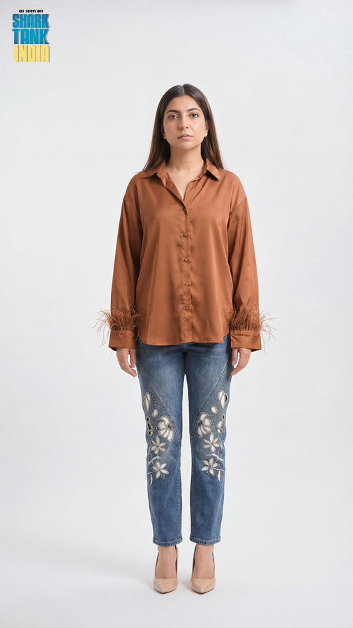 Woman wearing a brown shirt and blue jeans with floral embroidery on a white background