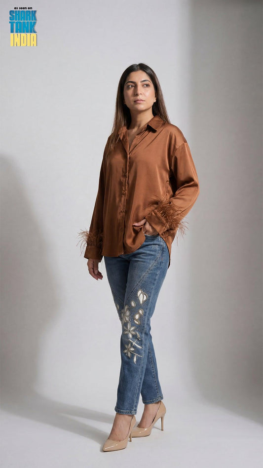 Woman wearing a brown satin shirt and blue jeans with cut-out details on a white background