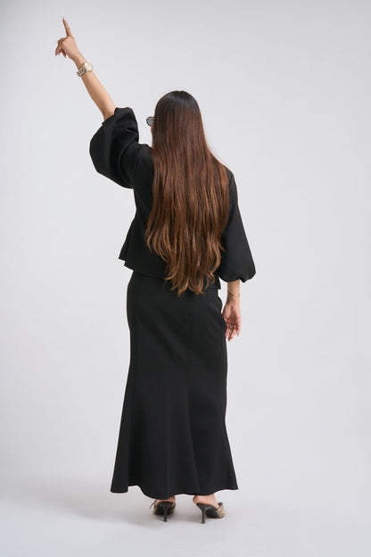 Woman in a black outfit pointing to the side against a white background