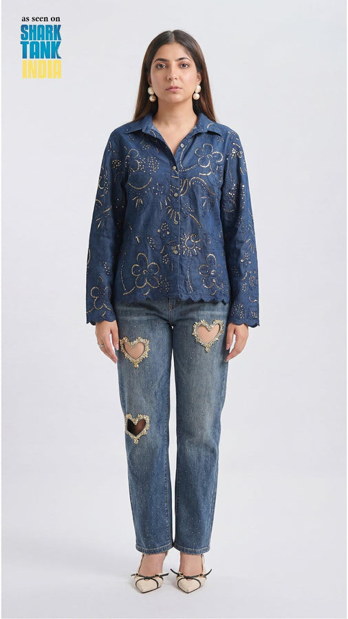 Woman wearing a blue embroidered jacket and distressed jeans on a white background