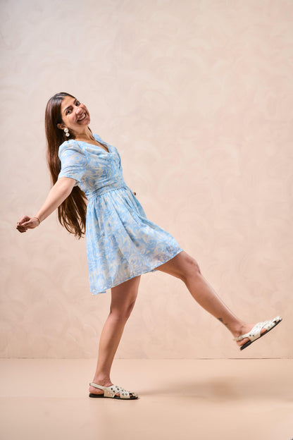 Woman in a light blue floral dress posing against a beige background