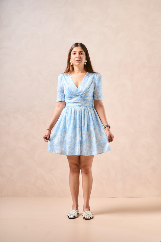Woman wearing a light blue dress with a subtle pattern against a beige background