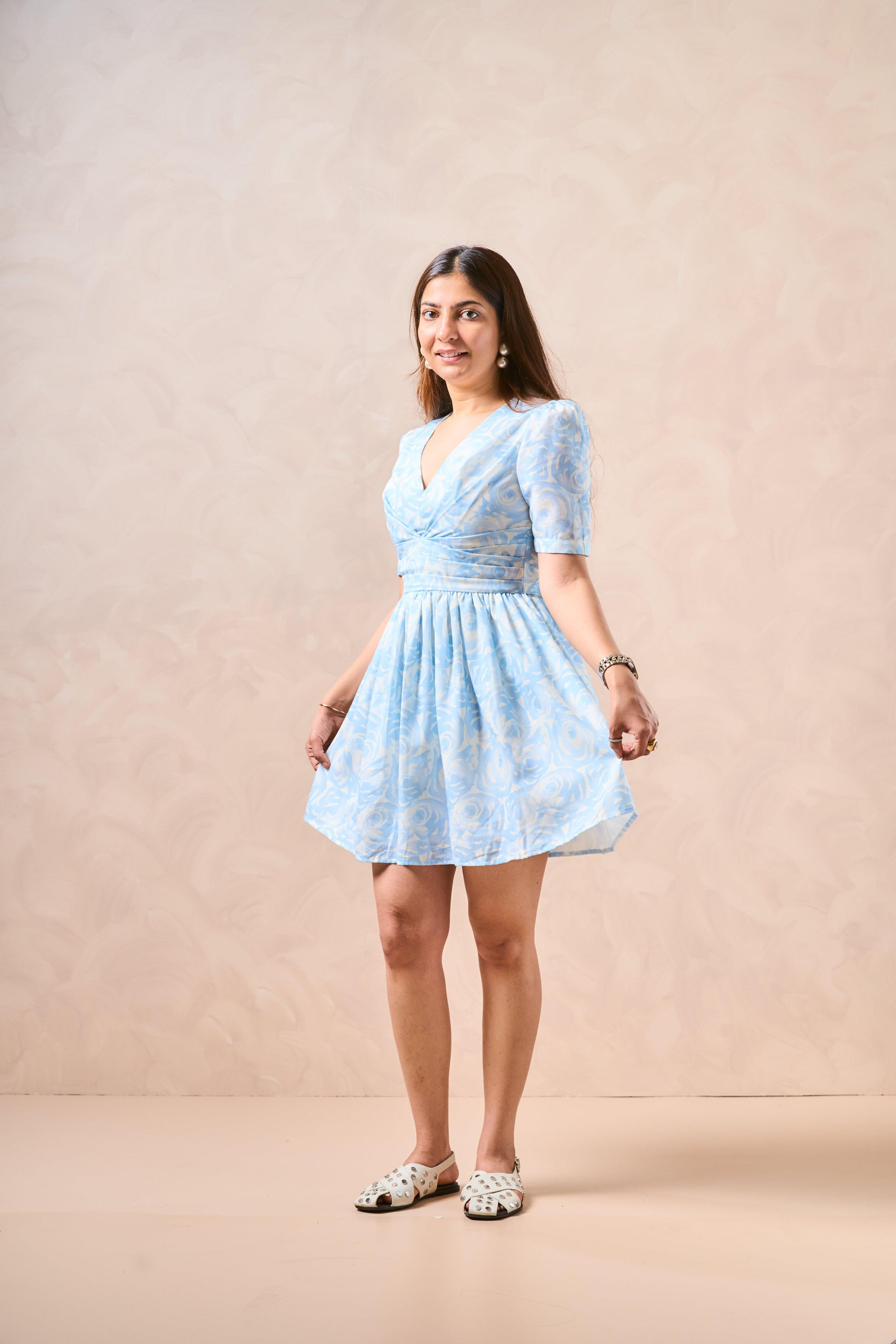 Woman wearing a light blue dress with white patterns against a beige background