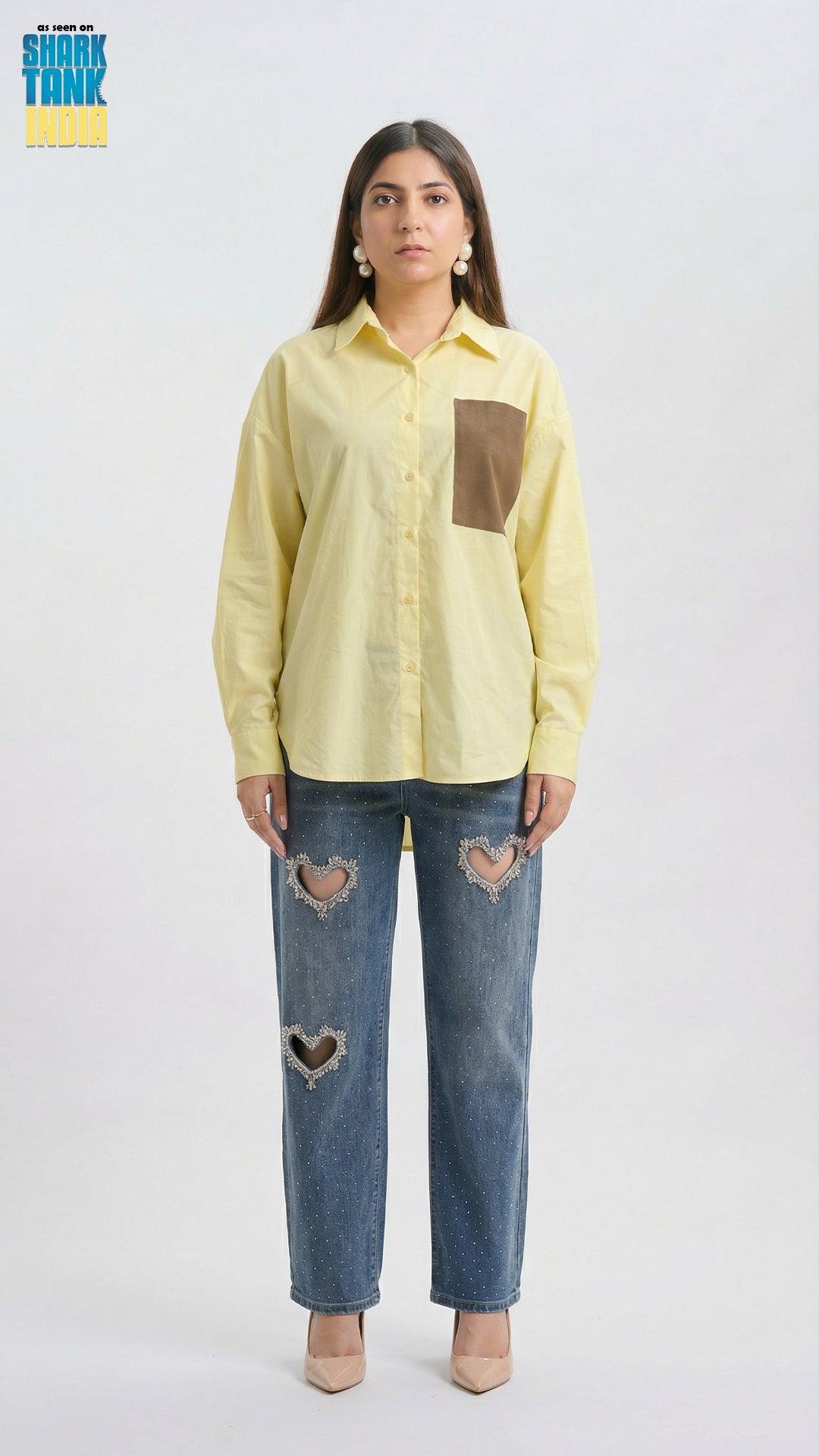 Woman wearing a light yellow shirt with a brown pocket and blue jeans with heart cutouts on a white background.