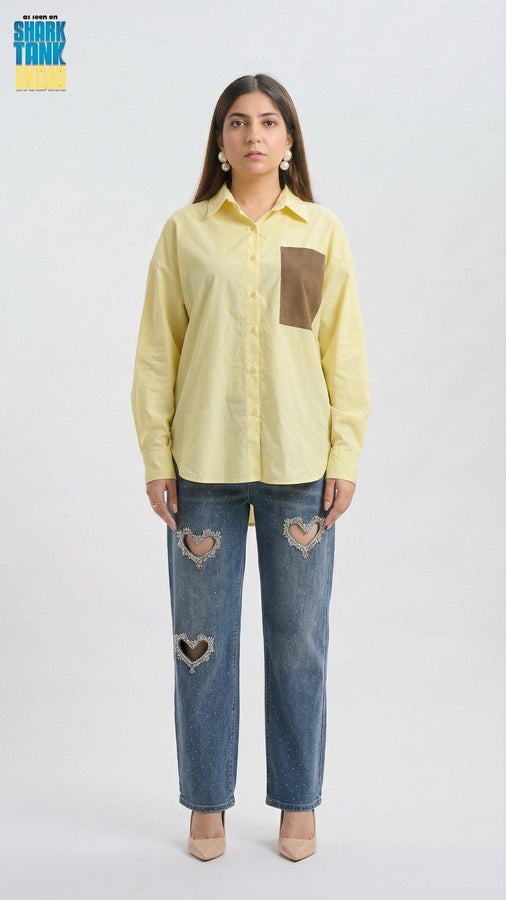 Woman wearing a light yellow shirt with a brown pocket and blue jeans with heart cutouts on a white background.