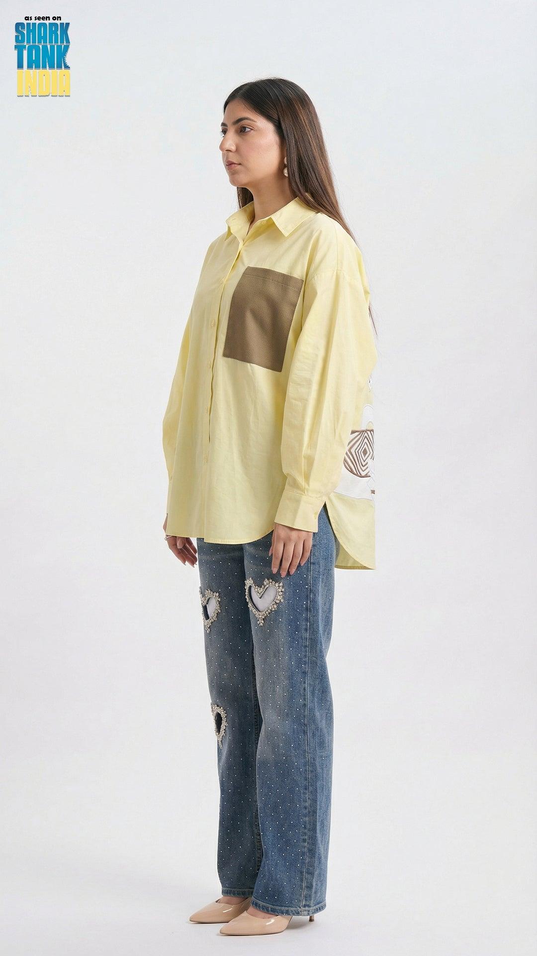 Woman wearing a light yellow shirt with a brown square design and blue jeans on a white background