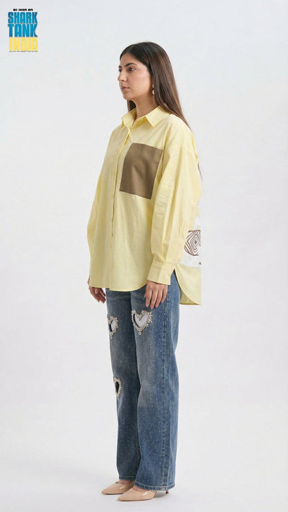 Woman wearing a light yellow shirt with a brown square design and blue jeans on a white background