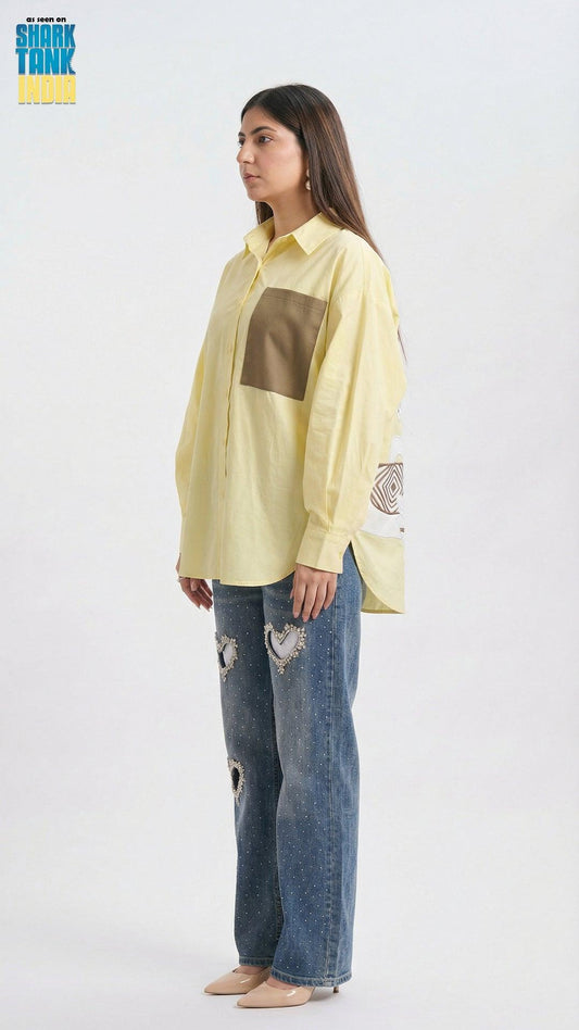 Woman wearing a light yellow shirt with a brown square design and blue jeans on a white background