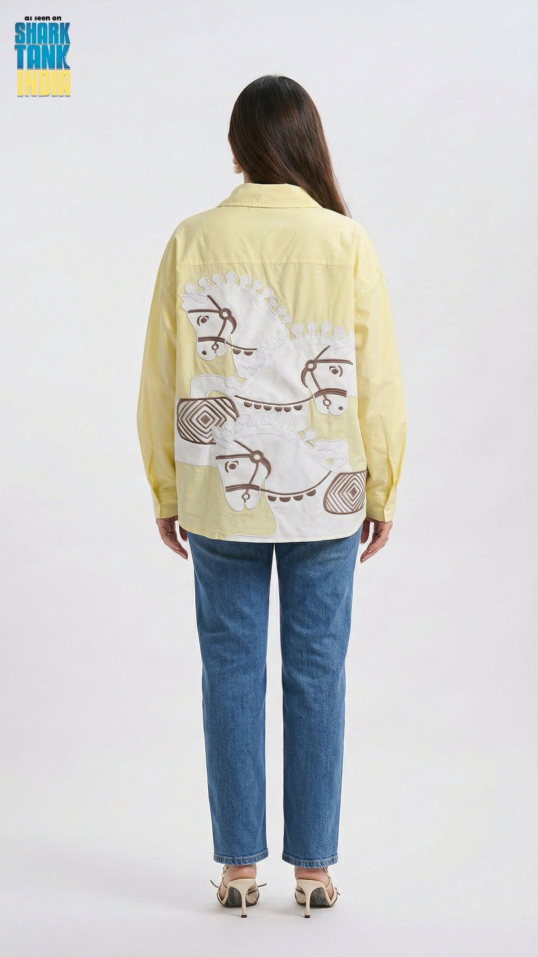 Person wearing a light yellow shirt with a graphic design on the back, standing against a white background.