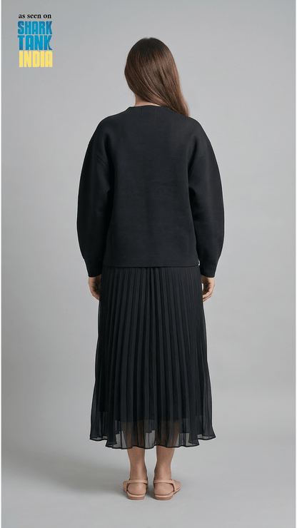Person wearing a black sweater and black pleated skirt on a gray background with 'Shark Tank India' logo.