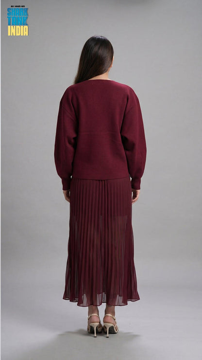 Woman wearing a maroon outfit with a pleated skirt on a gray background