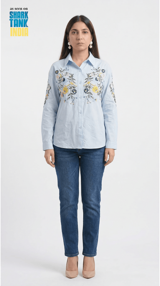 Woman wearing a light blue embroidered shirt and dark blue jeans on a white background